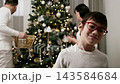Family decorates Christmas tree with ornaments and lights, while a child smiles and enjoys the moment 143584684