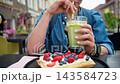 Woman Enjoying Iced Matcha Tea Through A Straw And Waffles With Cream And Berries Outside 143584723