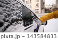 Woman Brushing Fresh Snow Off Car Windows With A Brush On a Parking In Winter 143584833