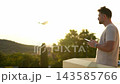 Enjoying the sunset while controlling a drone in a serene outdoor setting 143585766