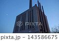 Large industrial power plant building with tall smokestacks under a clear blue evening sky and visible moon. Urban industrial architecture and energy infrastructure create a dramatic city industry 143586675