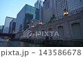 Downtown office towers rise above the Chicago Riverwalk during dusk in Chicago, Illinois. Urban waterfront scene with illuminated riverfront lights, bridge structures, reflections, and modern 143586678