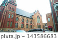 Large historic brick church building with gothic architecture in a quiet urban neighborhood. Traditional city street with parked cars, old brick buildings, and religious architecture in daylight. 143586683