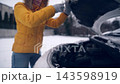 Female Driver Opens The Car Engine Hood Covered By Snow In The Parking Lot 143598919