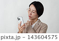 A middle-aged businesswoman thinking with her smartphone in hand, against a white background. 143604575