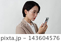 A middle-aged businesswoman struggling with her smartphone; white background. 143604576