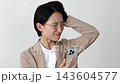 A middle-aged businesswoman with her smartphone in her hands, holding her head in her hands, against a white background. 143604577
