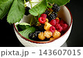 Fresh garden berries arranged in white ceramic bowl on elegant black background 143607015