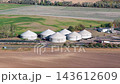 Aerial drone view of biogas production facility with large anaerobic digesters and agricultural fields in Germany. Renewable energy plant converts organic waste into sustainable fuel and electricity 143612609