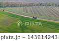 Aerial drone view shows tanker truck driving along rural road between green agricultural fields in Germany. Scenic autumn countryside reveals farmland, cultivated soil, trees and transport logistics 143614243