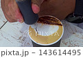 Barista drawing a face pattern with chocolate syrup on a cappuccino milk foam creating creative latte art close up. 143614495