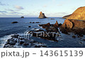 A closer aerial view holds on the Benijo sea stacks as surf breaks white around their base. A tighter angle on Tenerife's landmark rock formation for travel content. 143615139