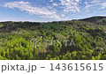 Elevated aerial perspective over hillside village featuring patchwork farmland patterns, scattered houses, and prominent church steeple. 143615615