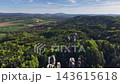 High-altitude drone view shows dense woodland covering rolling hills, rugged rock spires standing out in foreground, and patchwork fields leading to villages and distant towns under clouds. 143615618