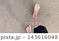 Top-down first person view of male legs and bare feet walking barefoot on sand beach with wet sandy ground and footprints on sea coast. POV walk. Summer holiday vacation leisure and recreation time. 143616048