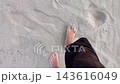 Top-down first person POV of bare male feet walking barefoot on sand beach with white sandy ground and footprints on surface. Point of view walk. Summer vacation holiday leisure and relaxation time. 143616049