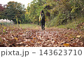 A fixed shot of a female hiker walking along a leaf-covered trail in the Shibusawa Hills in autumn, from behind. 143623710