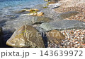 Rocks and water at a beach with pebbles near the shore in bright sunlight 143639972
