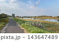 秋の河川敷、川沿いにまっすぐ延びる舗装された遊歩道を歩く風景 143647489
