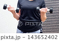 A person is exercising with dumbbells in a home environment. They perform various movements to work out their arms and shoulders 143652402