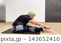 Person performs a series of stretching exercises on a yoga mat in a home setting. The focus is on improving flexibility and core strength 143652410