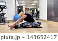 A person performs a series of stretching exercises in a gym setting focusing on flexibility and body movement 143652417