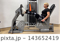 A woman uses a gym machine to perform leg exercises while maintaining proper form. She focuses on lifting her legs in a controlled manner 143652419