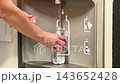 A person is filling a water bottle at a water refill station located in a public space. The water flows from the dispenser 143652428