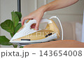 Woman turning temperature control dial on electric iron. Laundry care and household chores 143654008