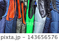 Numerous colorful vests are displayed in a clothing store, showcasing a variety of styles and fabrics. The vibrant colors and textures create a visually appealing arrangement. 143656576