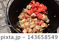 Chunks of meat fried with onions and tomatoes in a cast iron cauldron outdoors. 143658549