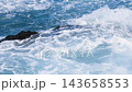 Waves crashing over rugged black volcanic rocks, creating white foam, splashes, and flowing seawater. 143658553