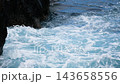Waves crashing over rugged black volcanic rocks, creating white foam, splashes, and flowing seawater. 143658556