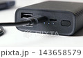 Close-up of a black portable power bank charging through a connected cable, showing usb ports, battery indicator lights, and the power button on a white background 143658579