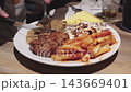 A person cutting into a steak dinner plate served with French fries, salad, and toast at a restaurant table. 143669401