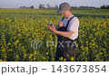 Rapeseed oil production. An agronomist farmer enjoys scent of rapeseed blossoms while standing in a rapeseed field, holding a bottle of oil, rural farming quality control, healthy ingredient sourcing 143673854