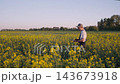 Agronomist inspecting rapeseed plants and recording field data in blooming crop field at golden hour with wide rural landscape, calm sky and careful yield planning in focused agricultural work scene. 143673918
