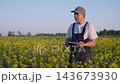 Agronomist in blooming rapeseed field studies crop growth and writes notes while checking plants under warm evening light, focused on yield planning and harvest assessment and rural farm management, 143673930
