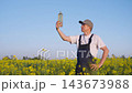 Agronomist or farmer proudly examines a bottle of rapeseed oil while standing in a rapeseed field. Rapeseed oil production and farming concept. Small business, rapeseed cultivation and processing. 143673988