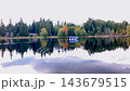 Peaceful lake scene with colorful trees, house reflections, and a small boat on calm water. 143679515