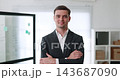 Portrait of positive businessman crosses arms in corporate workspace. Successful young employee builds career at commercial company. Financial professional 143687090