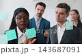 Portrait of business team members apply stickers with marketing ideas onto glass wall. Multiethnic colleagues seeks solutions for development in office 143687091
