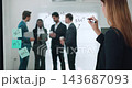 Caucasian businesswoman writes Meeting on glass board as multicultural colleagues discuss plan. Woman adds word to workflow map as records ideas in office room 143687093
