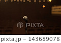 Camera slowly pushes in on a single microphone on a stand, with an empty dimly lit auditorium and warm bokeh string lights in the soft focus distance 143689078