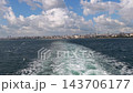 Vessel Wake on the Sea Beneath Cumulus Clouds with a Distant City Skyline 143706177