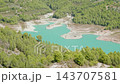 Aerial turquoise reservoir winding through pine covered hills with exposed sandy peninsulas under bright daylight, calm scenic landscape view from above, summer nature panorama over evergreen forest 143707581