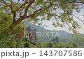 Mediterranean mountain valley framed by leafy tree branches with limestone cliffs and distant forested ridges in soft midday light on summer day of calm scenery. 143707586