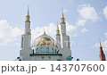 Mosque with reflective golden dome and four slender minarets under pale blue sky, upward view emphasizing shimmering metal tiles and bright daylight reflection, serene architectural scene 143707600