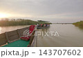 Wooden tour boat full of passengers gliding along calm river channel at sunset with foreground bow of second boat view from low angle and soft evening light on marshland scene 143707602