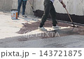 A construction worker applies a bituminous waterproofing layer to an exposed floor surface using a paint roller. This protective coating prevents rainwater leakage into the structure below. 143721875